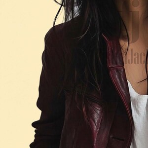 May include: A burgundy leather jacket with a classic button-up design. The jacket has a tailored fit and a rich, deep color. The image shows the jacket's shoulder and lapel details, suggesting a stylish outerwear piece.