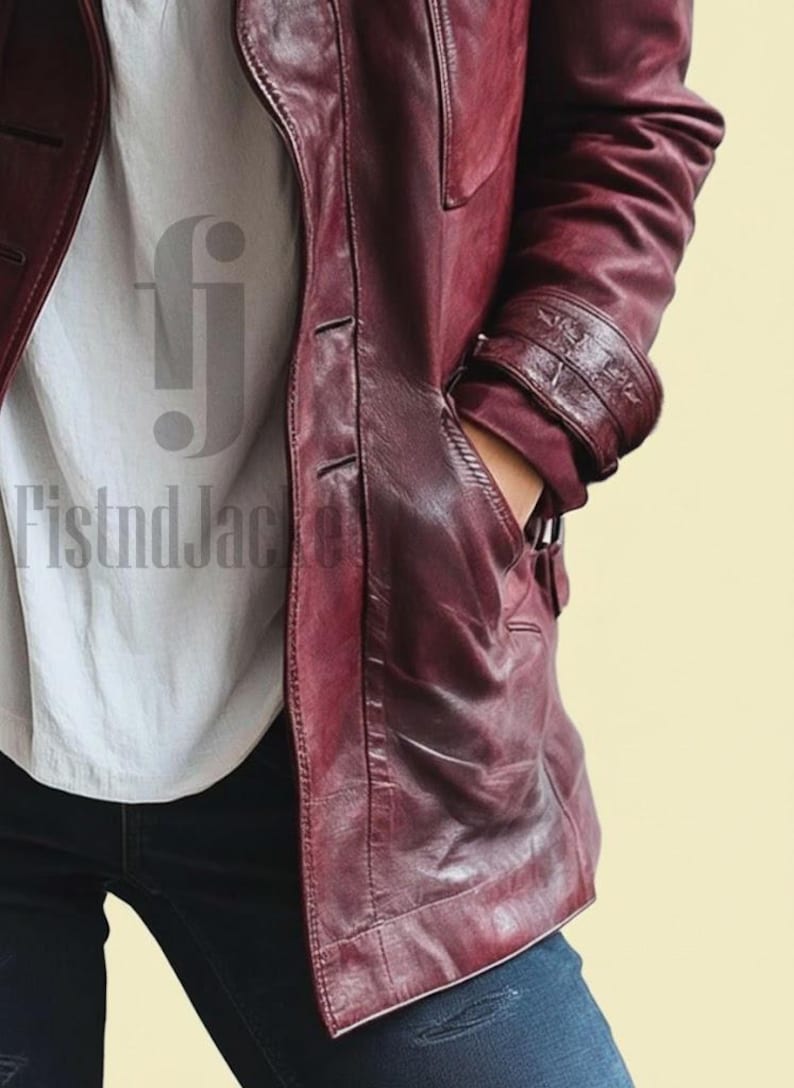 May include: A burgundy leather jacket with a buttoned front, side pockets, and a notched collar. The jacket has a tailored fit and features detailed stitching. The sleeves have decorative cuffs. The jacket is worn over a white shirt and blue jeans.