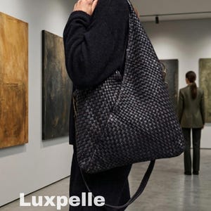 May include: A black woven leather shoulder bag with a long strap. The bag is carried over the shoulder. The word "Luxpelle" is written in white at the bottom of the image. The background includes abstract art and a person.