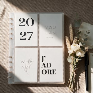 Könnte beinhalten: Ein spiralgebundenes Fotoalbum mit transparentem Einband, das vier weiße Karten mit schwarzem Text enthält. Die Karten zeigen die Zahlen 20 27, die Worte YOU CAN END OF STORY, WHY NOT mit einer Blattillustration und J' ADORE. Ein kleiner Strauß getrockneter Blumen liegt daneben.