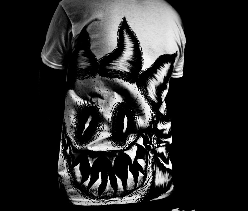 K&ouml;nnte beinhalten: Graues T-Shirt mit einer gro&szlig;en, detaillierten Schwarz-Wei&szlig;-Illustration eines Monstergesichts auf dem R&uuml;cken. Das Design umfasst spitze Z&auml;hne, gro&szlig;e Augen und spitze Ohren, was eine auff&auml;llige und kantige &Auml;sthetik erzeugt.