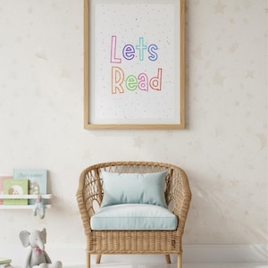 May include: A wooden framed print with the words "Lets Read" in colourful letters hangs above a wicker chair with a blue cushion. A stuffed elephant and books are nearby, suggesting a children's reading area. The room has a neutral colour palette.