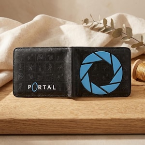 Può includere: Portafoglio nero a due ante con la scritta "PORTAL" in bianco e blu. Il portafoglio presenta un design blu ad apertura sul lato destro. L'interno presenta un motivo ripetuto di piccole figure. Il portafoglio è realizzato in materiale strutturato.