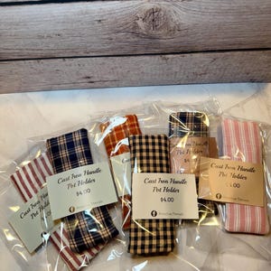 May include: Several cast iron handle pot holders in a variety of patterns, such as plaid and striped. Each is packaged in a clear plastic bag with a tag that reads "Cast Iron Handle Pot Holder".