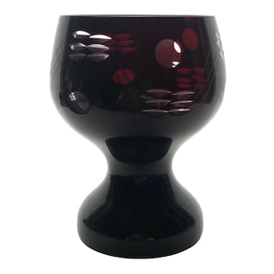 May include: A dark red glass goblet with a wide bowl and a flared base. The bowl is decorated with a geometric pattern of circles and lines.