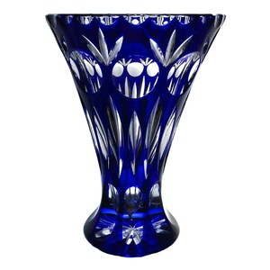 May include: A cobalt blue crystal vase with a flared top and a round base. The vase features intricate cut patterns, including circles and vertical lines, creating a decorative design. The vase is approximately 10 inches tall.