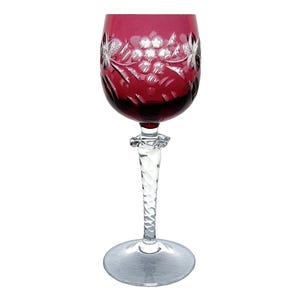 May include: A ruby red wine glass with a clear, twisted stem and a round base. The bowl of the glass features a cut floral design. The glass is made of crystal and is designed for serving wine.