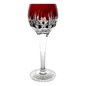 Può includere: Un singolo ed elegante calice da vino con una coppa rosso rubino e un lungo stelo trasparente. Il bicchiere presenta intricati disegni in cristallo tagliato a stella e geometrici. La base è rotonda e anch'essa tagliata con un motivo a stella.