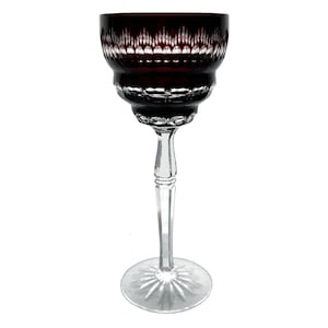 May include: A tall, elegant wine glass. The deep burgundy bowl has a detailed, textured pattern, and the clear stem and base are intricately cut. The base has a starburst design. The glass is designed for serving wine.