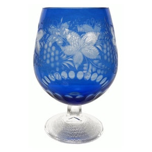 May include: A cobalt blue glass goblet with a cut glass design of grapes and leaves. The goblet has a round bowl and a clear glass stem and base.