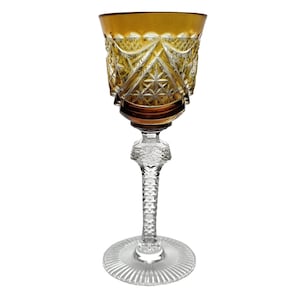 Może przedstawiać: Szklanka do wina na nóżce, wykonana z przezroczystego szkła z wygrawerowanym wzorem. Kubek szklanki jest w kolorze bursztynowym.