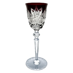 Puede incluir: Una sola copa de vino elegante con un cuenco rojo rubí y un tallo y base de cristal transparente y tallado intrincadamente. La copa presenta patrones detallados y un tallo largo y esbelto, ideal para ocasiones formales.