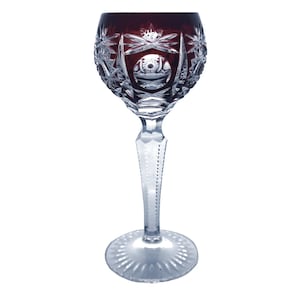 Op de afbeelding: Een helder glazen wijnglas met een diepe rode tint en een ingewikkeld geslepen glasontwerp. Het glas heeft een lange steel en een brede, uitlopende voet.