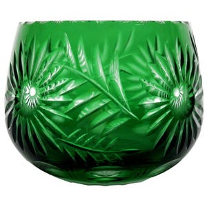 May include: A green, cut-glass bowl with a rounded shape. The bowl features a detailed pattern of radiating lines and leaf-like shapes, creating a textured surface. The glass has a deep emerald color, and the design is symmetrical, with the pattern repeating around the bowl.