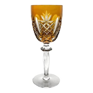 May include: A clear glass wine goblet with a cut crystal design. The goblet has a amber colored base and stem.
