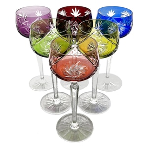 May include: A set of six coloured wine glasses. Each glass is a different colour: purple, red, blue, green, yellow, and orange. The glasses have a clear stem and base, and a starburst design on the bowl.