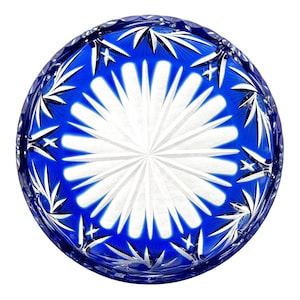 Puede incluir: Un cuenco redondo de cristal tallado con un exterior azul vibrante y un patrón blanco en forma de estrella en el centro. El borde del cuenco presenta un patrón repetitivo de cortes en forma de estrella. El cuenco probablemente se utiliza con fines decorativos.