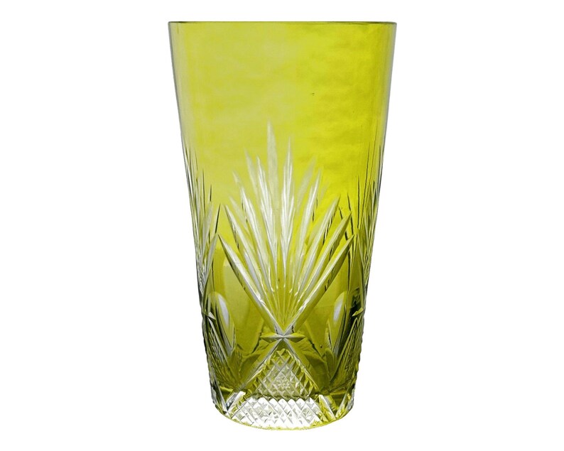 May include: A tall, chartreuse-colored glass with a cut-glass design. The glass features a pattern of vertical lines and diamond shapes, creating a textured appearance. The glass is ideal for serving beverages.