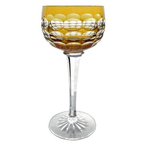 May include: A single amber-colored wine glass with a clear, long stem and a circular base. The bowl of the glass has a textured, bubble-like pattern. The glass is designed for serving wine or other beverages.