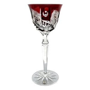 Könnte beinhalten: Ein einzelnes, elegantes Weinglas mit einer rubinroten Schale und einem klaren, aufwendig geschnittenen Stiel und Fuß. Die Schale weist detaillierte, geätzte Muster und ein dekoratives Design auf. Das Glas besteht aus Kristall und steht vor einem weißen Hintergrund.