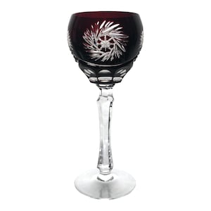 Puede incluir: Una copa de vino tinto oscuro con tallo y base transparentes. La copa tiene un diseño de cristal tallado.