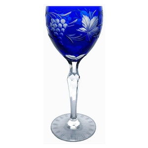 May include: A cobalt blue wine glass with a clear, faceted stem and base. The bowl is etched with a grape and leaf design. The glass is designed for serving wine.