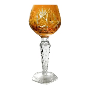 May include: A clear glass goblet with a cut crystal design. The goblet has a wide bowl and a tall, slender stem. The bowl is amber in color.