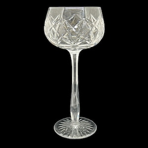 Puede incluir: Una copa de vino de cristal transparente con un tallo largo y una base redonda. El cuenco de la copa presenta un patrón de corte de diamante. La base tiene un diseño de estrella. La copa está sobre un fondo negro.