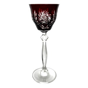 Può includere: Un bicchiere da vino a stelo in vetro trasparente con una coppa di colore rosso scuro. La coppa è decorata con un motivo in cristallo tagliato.