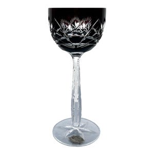 May include: A clear glass wine glass with a dark purple stem and base. The glass has a cut crystal design and is decorated with a starburst pattern.