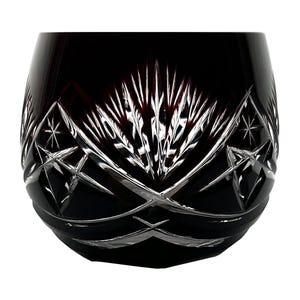 Può includere: Un bicchiere di cristallo rosso scuro senza stelo con intricati motivi a stella e tagli geometrici. Il bicchiere ha una forma arrotondata ed è progettato per migliorare l'esperienza di consumo. Il design in cristallo tagliato riflette la luce.