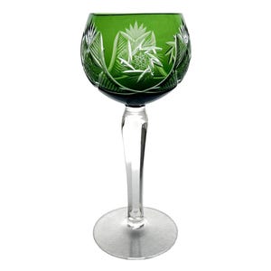 May include: A green crystal wine glass featuring detailed etched floral patterns. The glass has a rounded bowl, a clear stem, and a circular base. The intricate carvings and the deep green colour give the glass a classic, elegant appearance.