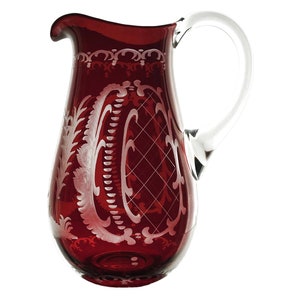 May include: A red glass jug with a clear glass handle. The jug has a white etched design of flowers and leaves.