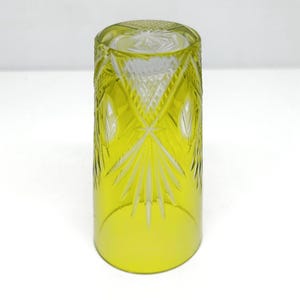 May include: A yellow-tinted, cylindrical glass with intricate cut patterns. The glass features a detailed design of diamond and fan-shaped cuts, creating a textured surface. The glass is suitable for beverages and adds a touch of elegance to any table setting.