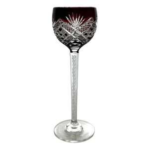 May include: A tall, clear glass with a deep red, cut-glass bowl and a long, clear stem with a cut-glass design. The glass has a wide, clear base.