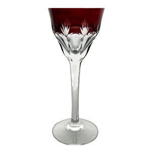 Könnte beinhalten: Ein klares Weinglas mit einem tiefroten Kelch und einem geschliffenen Kristallmuster. Das Glas hat einen langen, dünnen Stiel und einen breiten Fuß.