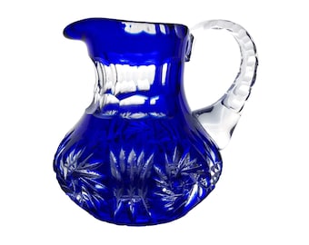 May include: A cobalt blue crystal pitcher with a clear, textured handle. The pitcher's body features a starburst pattern, and the rim is gently curved. This decorative pitcher is ideal for serving beverages.