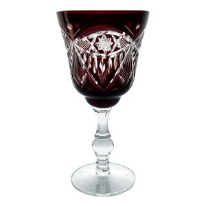 May include: A deep red wine glass with a cut crystal design. The glass has a clear stem and base.