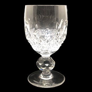May include: A clear glass wine glass with a cut crystal design and a round, faceted stem. The glass has a wide bowl and a delicate base.