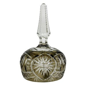 Puede incluir: Un tapón de botella de vidrio transparente con una parte superior cónica facetada y una base redonda de vidrio tallado. La base tiene un diseño de estrella con intrincados patrones tallados en color gris ahumado. El tapón está diseñado para una botella.