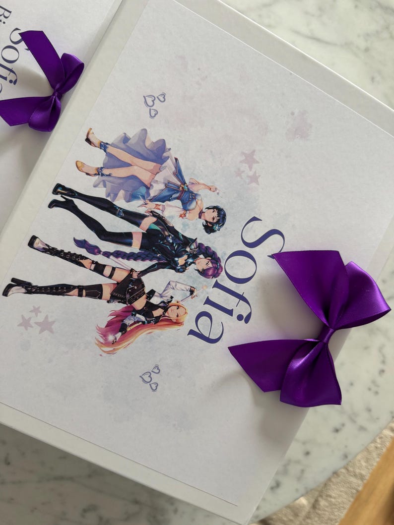 May include: A white rectangular box featuring a printed graphic of three anime-style characters in varied outfits, the name Sofia in dark blue text, and two decorative purple satin bows attached to the corners of the lid.