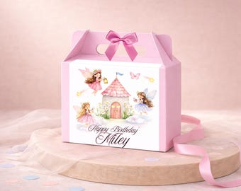 May include: A pink gable box with a bow on top, featuring a fairy castle illustration. The box has a label with fairies, a castle, and the text "Happy Birthday Miley". A pink ribbon and confetti are on the surface.