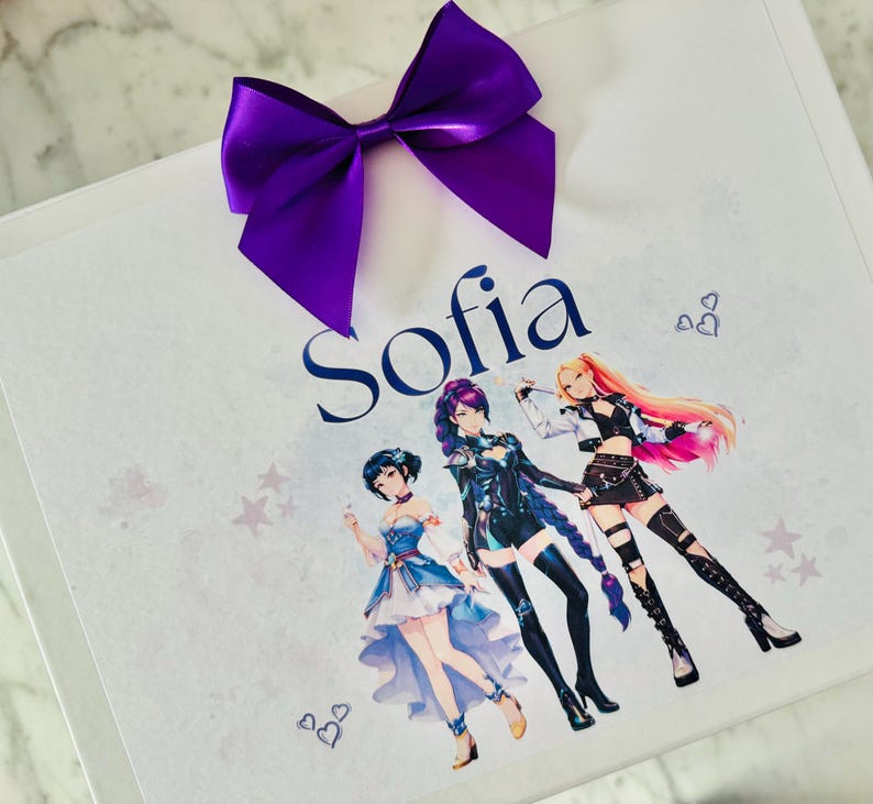 May include: A white rectangular gift box featuring a large purple satin bow at the top. The name Sofia is printed in dark blue script. Below the name are three anime-style characters in colorful outfits, surrounded by small heart and star icons.