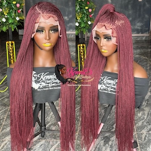 May include: A burgundy-colored braided wig with a lace front is displayed on a mannequin head. The wig features long, micro braids and is styled in two ways: flowing down and pulled up into a high ponytail. The mannequin is on a tripod stand. The text "Kenni's Hair Boutique" is visible.