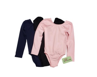 May include: Three long-sleeved leotards in navy blue, black, and pink. The leotards are made of a soft, stretchy fabric and have a scoop neck. The leotards are stacked on top of each other, with the pink leotard on top. The leotards have a tag that says "Prizm".