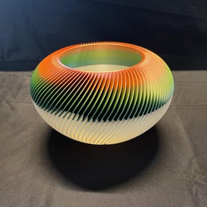 May include: A decorative bowl with a unique design. The bowl features a gradient of colors, transitioning from orange to green, and then to white. The bowl has a circular shape with a ribbed texture, creating a visually appealing aesthetic.