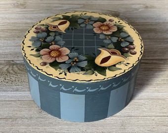 May include: A round, blue and white striped wooden box with a painted floral design on the lid. The lid features a yellow, cream, and brown floral pattern with a grid background.