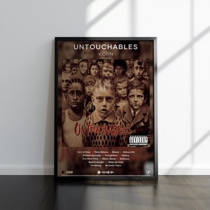 Puede incluir: Un póster de música enmarcado para el álbum Untouchables de Korn. La obra presenta un collage en tonos sepia de rostros de niños, el título del álbum en texto blanco y rojo, una etiqueta de Parental Advisory y una lista de canciones en blanco.
