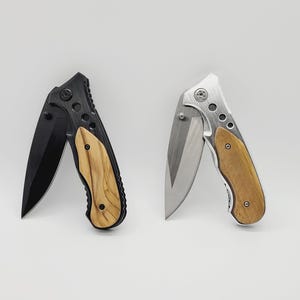 May include: Two open folding knives with wooden handles and metal blades. One knife has a black blade and frame, the other has a silver blade and frame. The blades are approximately 3 inches long.
