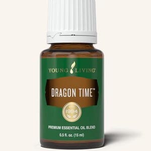 Puede incluir: Una botella de vidrio marrón de la mezcla de aceites esenciales premium Young Living Dragon Time. La botella tiene una etiqueta verde con el texto "DRAGON TIME" y "1994". La botella contiene 15 ml. La botella tiene una tapa blanca.